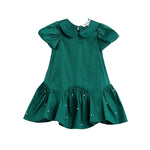 The Holly and Pearls Dress by Mabel + Honey is an emerald green, short-sleeve toddler dress featuring a solid design, Peter Pan collar, drop waist with a flared ruffled hem, and delicate pearl embellishments. The dress is presented against a white background.
