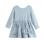 The Eva Dress Long Sleeve Textured A Line Bow Trim Dress by Mabel + Honey is a dusty blue cotton-blend girls’ dress featuring a textured knit pattern, long sleeves, a round neckline, and a flared skirt accented with three decorative bows on the front.