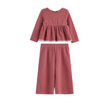 The Maribelle Two Piece Set by Mabel + Honey features a long sleeve polka dot peplum top and matching wide-leg pants in a dusty rose hue with small white spots, creating a playful yet chic look for girls.