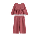 The Maribelle Two Piece Set by Mabel + Honey features a long sleeve polka dot peplum top and matching wide-leg pants in a dusty rose hue with small white spots, creating a playful yet chic look for girls.