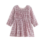 The Mabel and Honey Loretta Long Sleeve Floral Smocked Yoke A Line Dress is a pink, long-sleeved child’s dress with a gathered bodice and flared skirt, crafted from soft cotton gauze for comfort and shown on a white background.