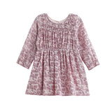 The Mabel and Honey Loretta Long Sleeve Floral Smocked Yoke A Line Dress is a pink, long-sleeved child’s dress with a gathered bodice and flared skirt, crafted from soft cotton gauze for comfort and shown on a white background.