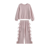 The Emma Two Piece Set Long Sleeve Textured Top And Wide Leg Pant Two Piece Set by Mabel + Honey showcases a light pink, textured knit ensemble with a long-sleeve top and matching wide-leg pants featuring bow-tied details and an elastic waistband, all presented against a white background.