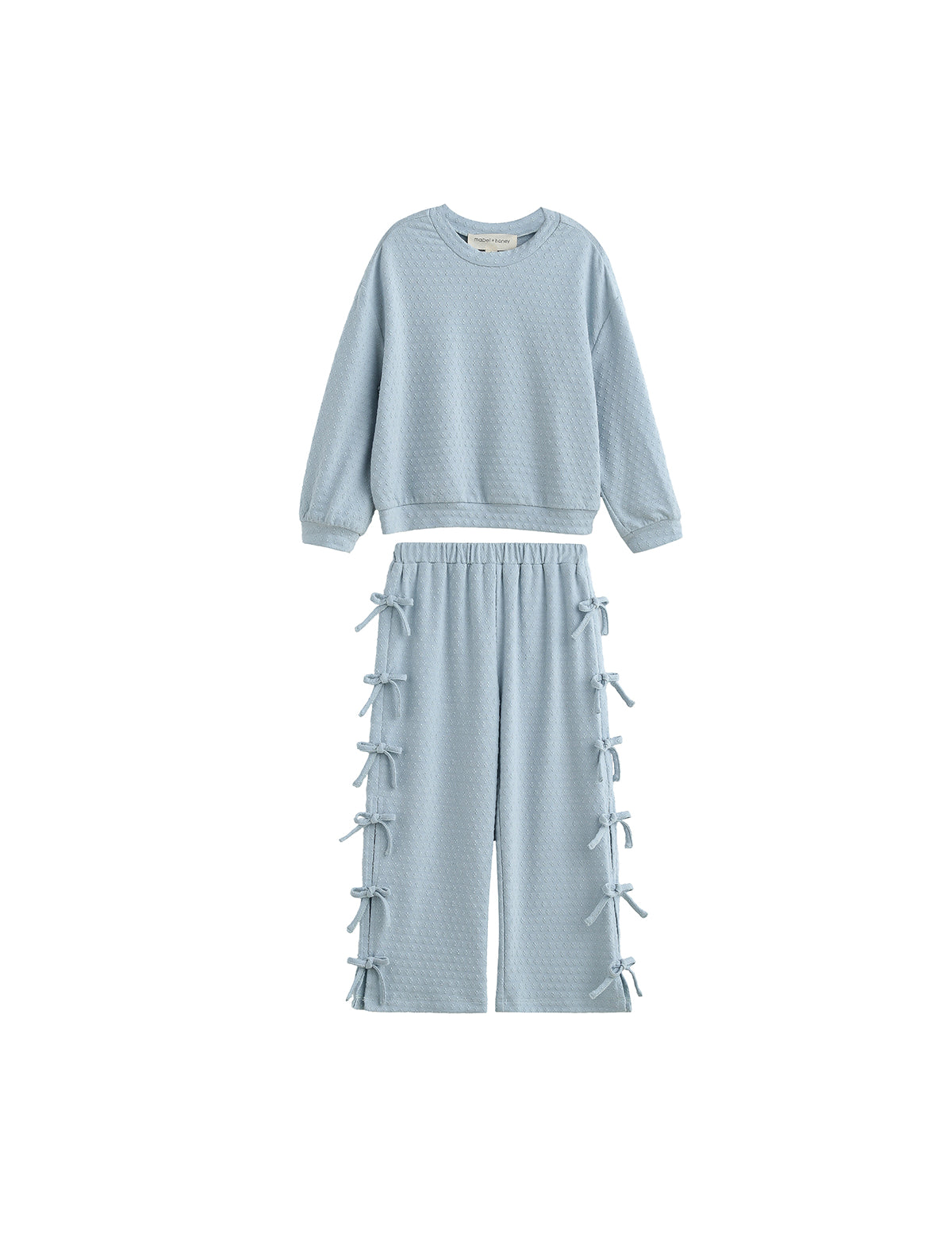 The Eva Two Piece Set Long Sleeve Bow Tie Detail Two Piece Set from Mabel + Honey features a powder blue textured design for children, including a long-sleeve top and wide-leg pants adorned with decorative bows along the sides. This two-piece set offers a relaxed, comfortable fit—perfect for all-day wear.