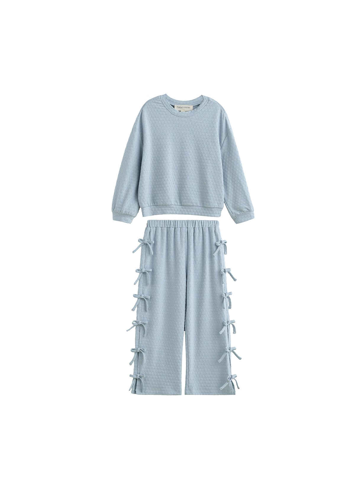 The Eva Two Piece Set Long Sleeve Bow Tie Detail Two Piece Set from Mabel + Honey features a powder blue textured design for children, including a long-sleeve top and wide-leg pants adorned with decorative bows along the sides. This two-piece set offers a relaxed, comfortable fit—perfect for all-day wear.