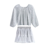 The Shimmer Shine Two Piece Set from Mabel + Honey features a light gray, metallic long sleeve solid top with elegant pleats and a gathered neckline, paired with a white sparkle dot tulle skirt detailed with subtle dots, tiered layers, and a wide waistband—an effortlessly chic ensemble perfect for any occasion.