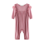 The Mabel + Honey Bowtiful Blush Romper Long Sleeve Solid Ribbed Bubble Leg Shoulder Tie Romper features a dusty rose hue with ribbed fabric, ruffled bubble legs, and charming shoulder ties. Snap buttons along the inseam provide easy dressing, while the romper is displayed on a white background.