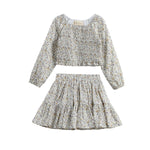 The Wildflower Dream Two Piece Set by Mabel + Honey showcases a long sleeve floral smocked top paired with a matching tiered mini skirt, both crafted from lightweight fabric adorned with a delicate small flower print. This charming set is displayed against a white background.