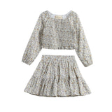 The Wildflower Dream Two Piece Set by Mabel + Honey showcases a long sleeve floral smocked top paired with a matching tiered mini skirt, both crafted from lightweight fabric adorned with a delicate small flower print. This charming set is displayed against a white background.