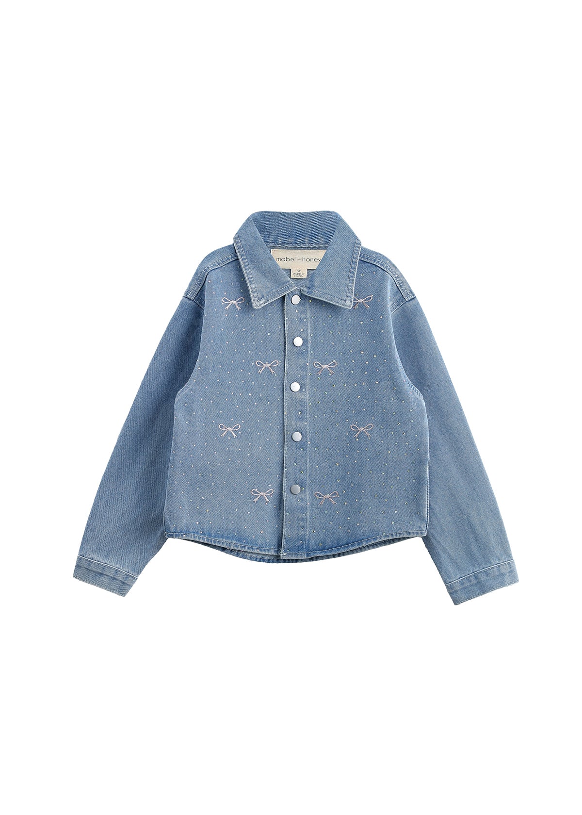 The Mabel + Honey Jacket Long Sleeve Print Rhinestone Bow Detail Cropped Denim Jacket features a light blue wash, classic collar, long sleeves, silver snap buttons, and sparkling rhinestone pink bows and dots embroidered on the front. The jacket is displayed laid flat on a white background.