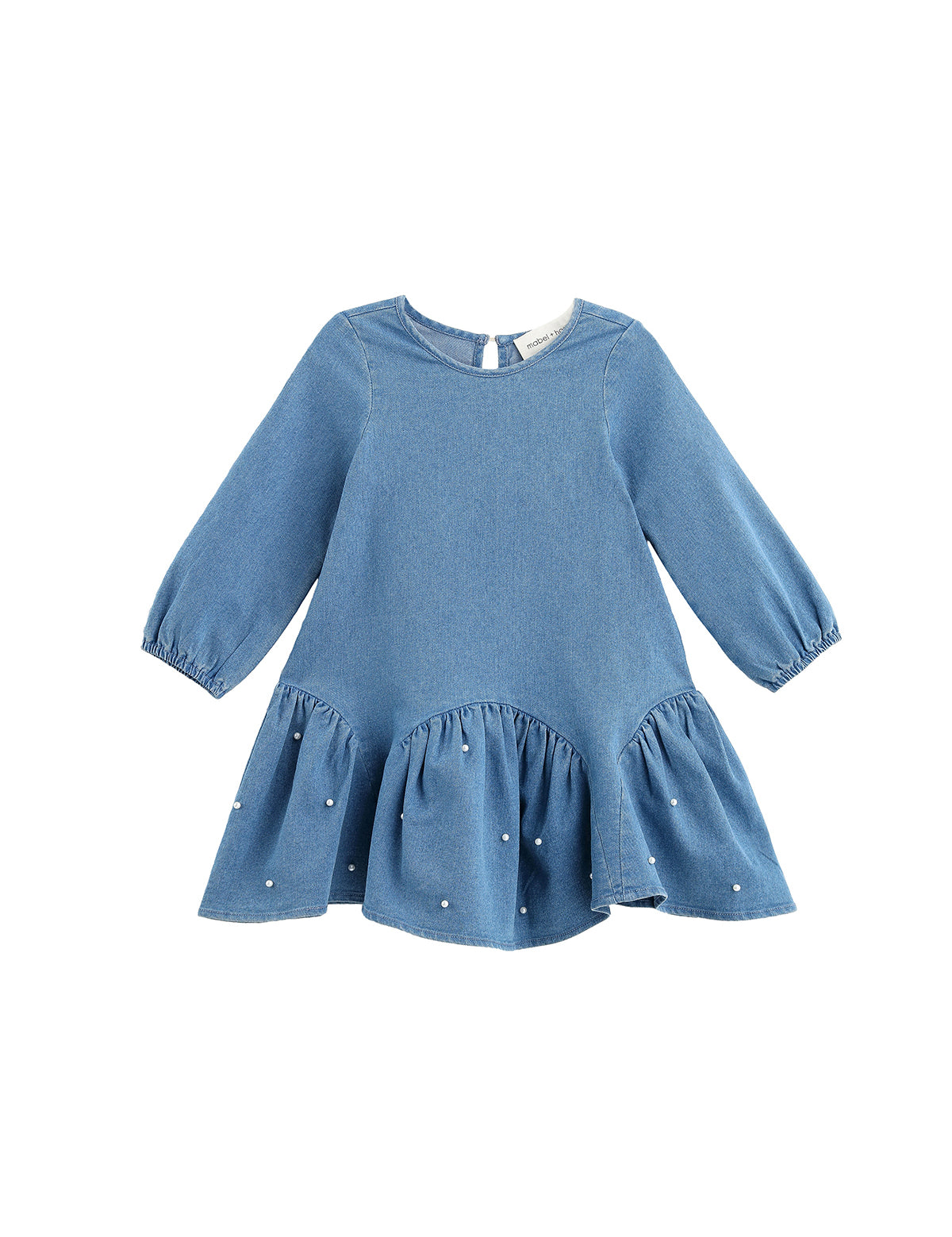 The Mabel + Honey Denim Doll Dress is a long-sleeve, solid chambray dress for children, featuring a dropwaist silhouette with a flared, ruffled hem accented by delicate white pearl embellishments and a classic round neckline.