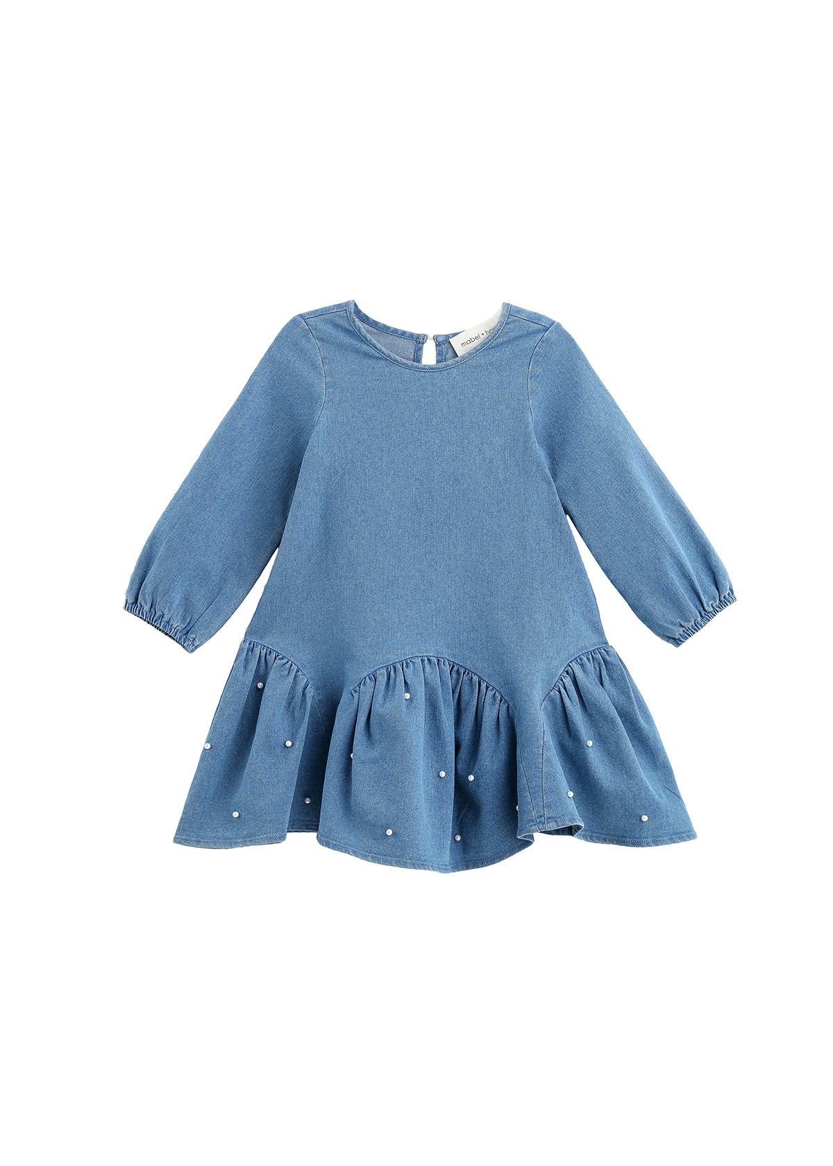 The Mabel + Honey Denim Doll Dress is a long-sleeve, solid chambray dress for children, featuring a dropwaist silhouette with a flared, ruffled hem accented by delicate white pearl embellishments and a classic round neckline.