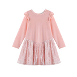 The Blushing Velvet Dress Long Sleeve Solid Sequin Skirt Party Dress by Mabel + Honey is a light pink girls’ party dress with ruffled shoulders and a shimmery sequined skirt. This charming piece features a sequin overlay, a round neckline, and is beautifully displayed against a white background.