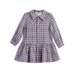 The Mabel and Honey Char Long Sleeve Plaid Collared Drop Waist Dress is a children’s dress made from soft brushed flannel. Featuring a classic plaid pattern in shades of purple, brown, and white, this lavender dress has long sleeves, a collared neckline, white buttons down the front, and a gathered drop waist skirt.
