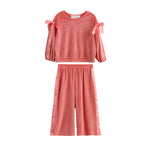 The Poppy Rose Long Sleeve Ribbed Bow Tie Top and Wide Leg Pant Set by Mabel and Honey features bow accents on the shoulders and a comfortable ribbed fabric, presented in a vibrant coral hue. This matching two-piece set includes a long sleeve top and wide-leg pants, both displayed against a white background.