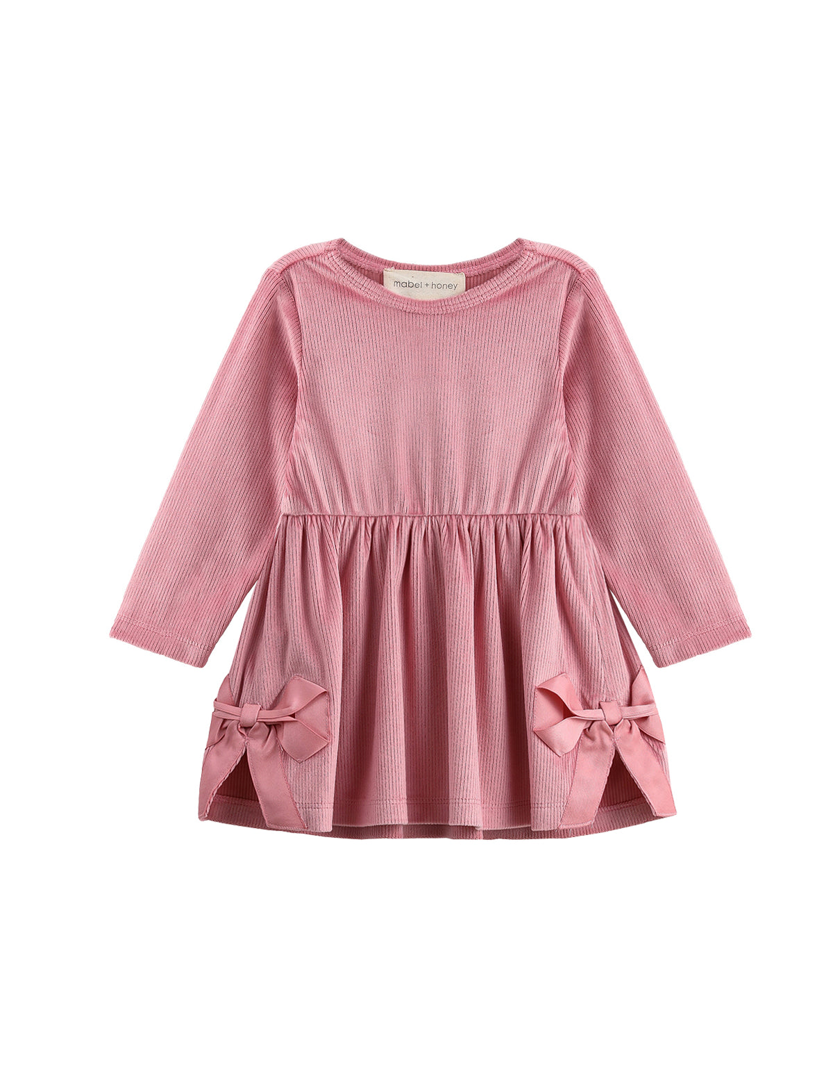 The Bowtiful Blush Dress Long Sleeve Solid A Line Bow Detail Dress by Mabel + Honey is a girls’ dress in blush pink, made of soft ribbed velour with long sleeves. It features a gathered waist and two large bows near the hem of the skirt, adding a charming touch, and is shown beautifully against a white background.