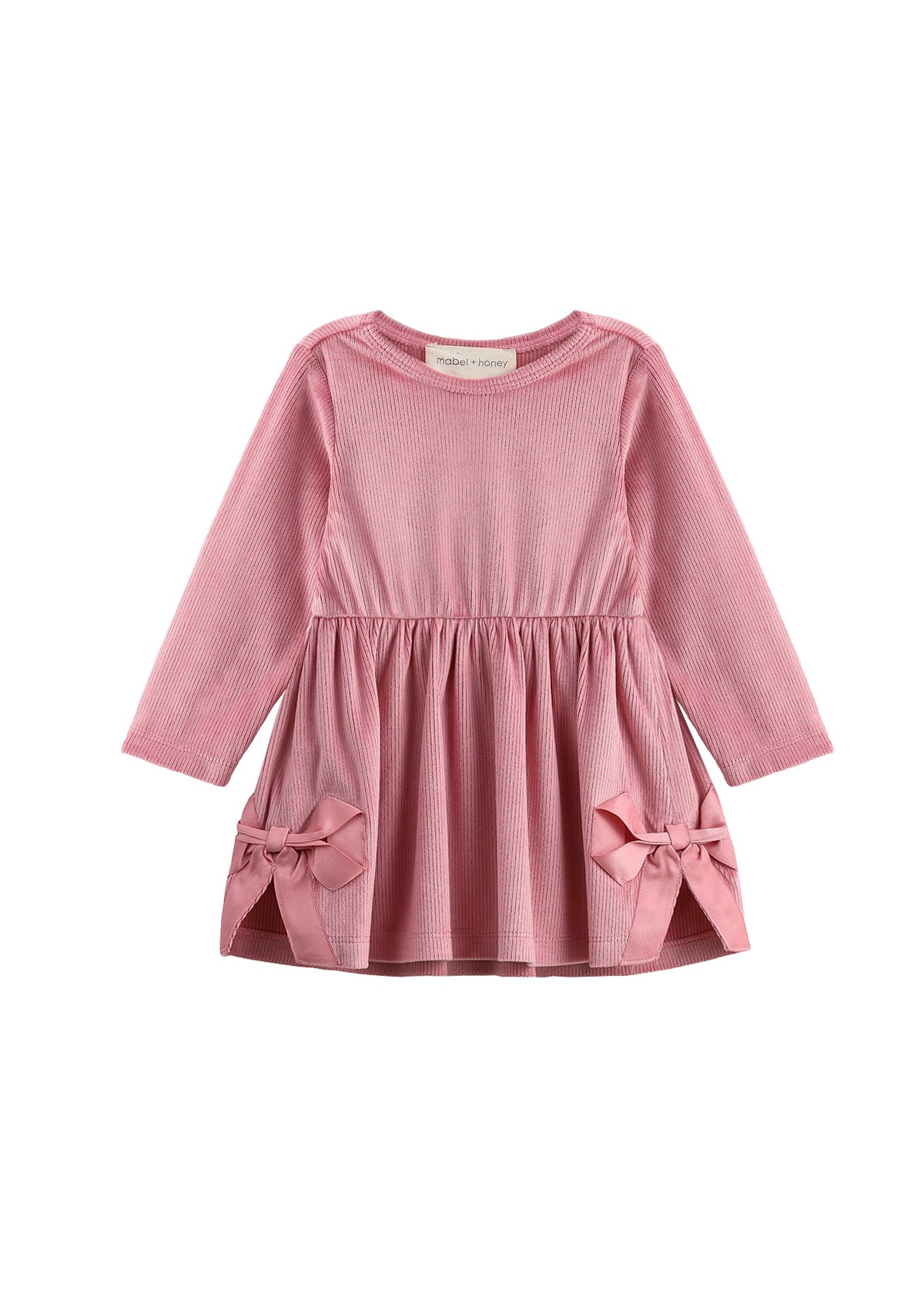 The Bowtiful Blush Dress Long Sleeve Solid A Line Bow Detail Dress by Mabel + Honey is a girls’ dress in blush pink, made of soft ribbed velour with long sleeves. It features a gathered waist and two large bows near the hem of the skirt, adding a charming touch, and is shown beautifully against a white background.