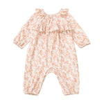 The Mabel and Honey Honey Petals Romper features long sleeves, a ruffled neckline, and a charming pink Honey Petals floral print on a white background. Crafted from soft stretch knit fabric, this straight leg romper is shown laid flat on a white surface.