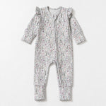 The Mabel + Honey Whimsical Wildflower Convertible Romper showcases long sleeves, straight legs, and charming ruffled shoulders, with a convenient zip-up front. Crafted from soft, stretchy knit fabric in a delicate pink and green ditsy floral print, this romper is displayed on a white background.