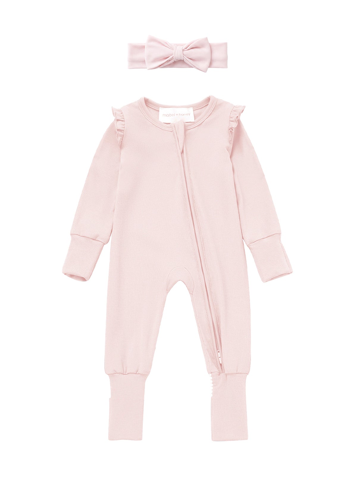 The Mabel + Honey Amelia Rose Convertible Romper features long sleeves, a zipper front, ruffled shoulders, and comes with a matching pink headband adorned with a bow, displayed flat on a white background.