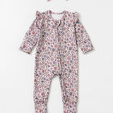 The Soft Meadow Long Sleeve Floral Print with Matching Headband by Mabel and Honey features a charming wildflower motif in soft pink, purple, and green tones. Crafted from cozy knit fabric, this adorable baby romper comes with ruffled shoulders and a coordinating headband, both beautifully displayed on a light background.
