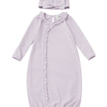 The Soft Meadow Newborn Gowns Long Sleeve Solid Gown with Matching Hat by Mabel + Honey features a lilac gown with ruffle trim along a diagonal front closure and an elasticized hem for easy changes. The set includes a matching hat accented with a front knot detail. Both pieces are crafted from soft fabric and are displayed on a white background.