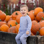 A young child in the Beckett and Bear Daniel Long Sleeve Solid Henley Cargo Jogger Set sits on a wooden box filled with pumpkins, smiling and laughing outdoors on a sunny day.