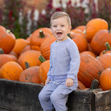 A young child in the Beckett and Bear Daniel Long Sleeve Solid Henley Cargo Jogger Set sits on a wooden box filled with pumpkins, smiling and laughing outdoors on a sunny day.